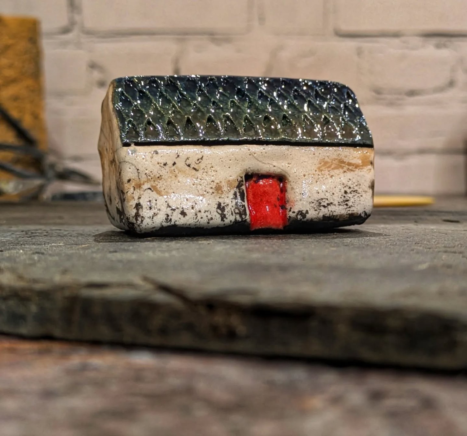 Finished raku croft house with pale walls, a dark glazed roof and a red door.