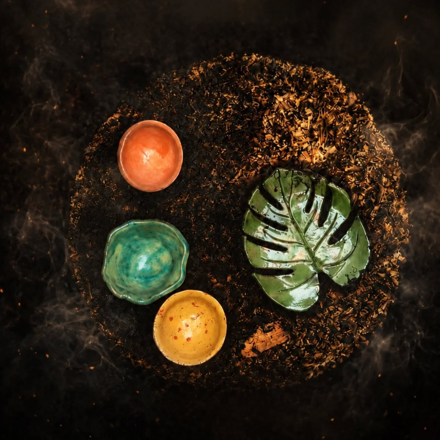 Small fired raku bowls and a green leaf-shaped dish arranged on the reduction bed