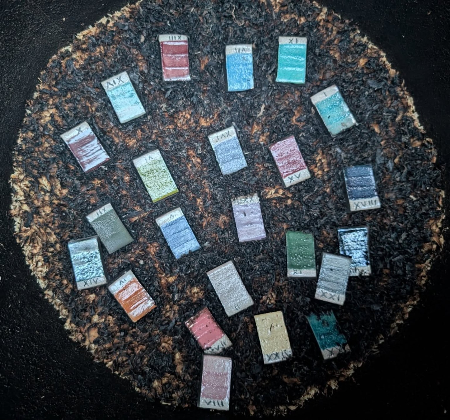 Fired raku glaze test tiles laid out on the charred sawdust reduction bed
