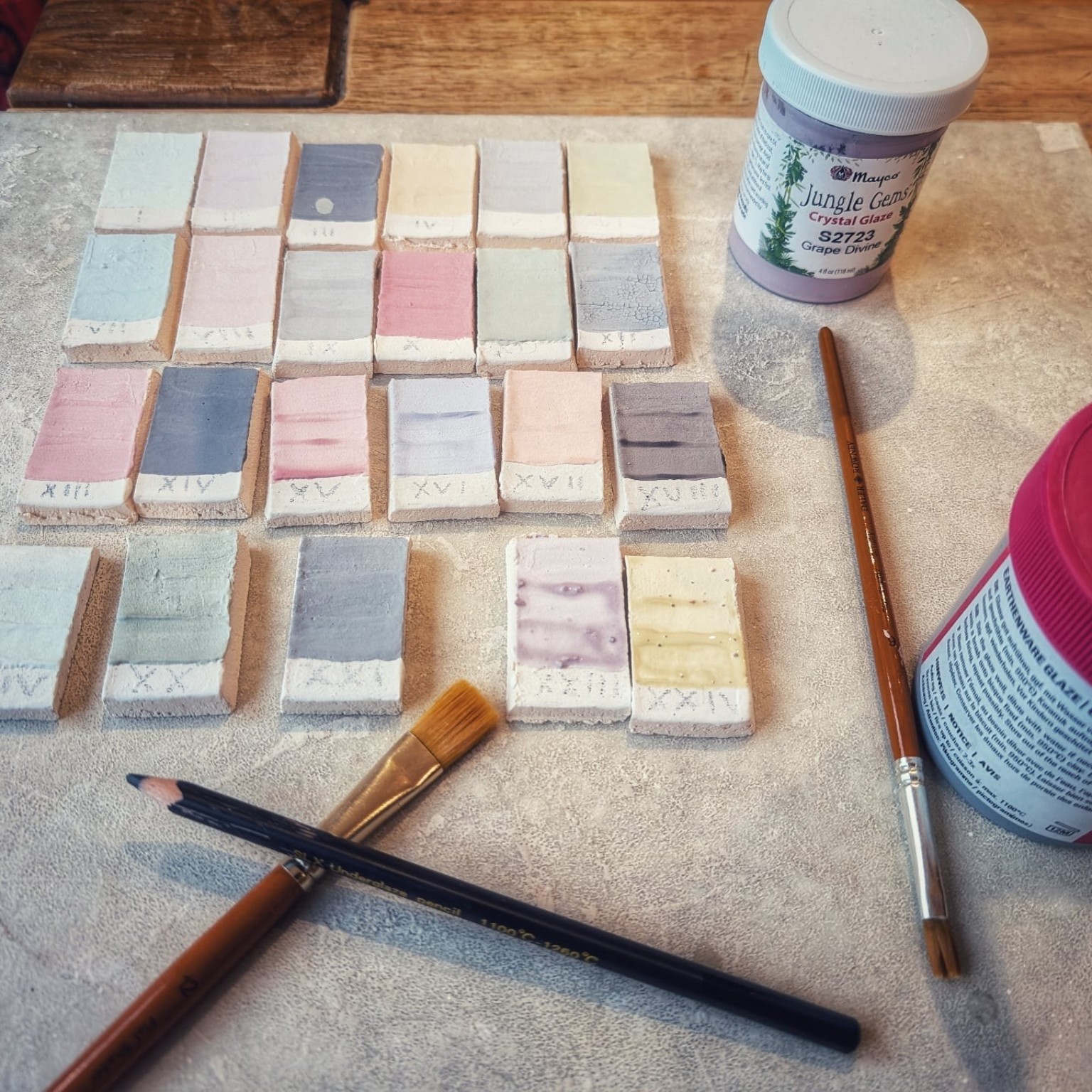 Rows of raku glaze test tiles with glaze jars and brushes before firing
