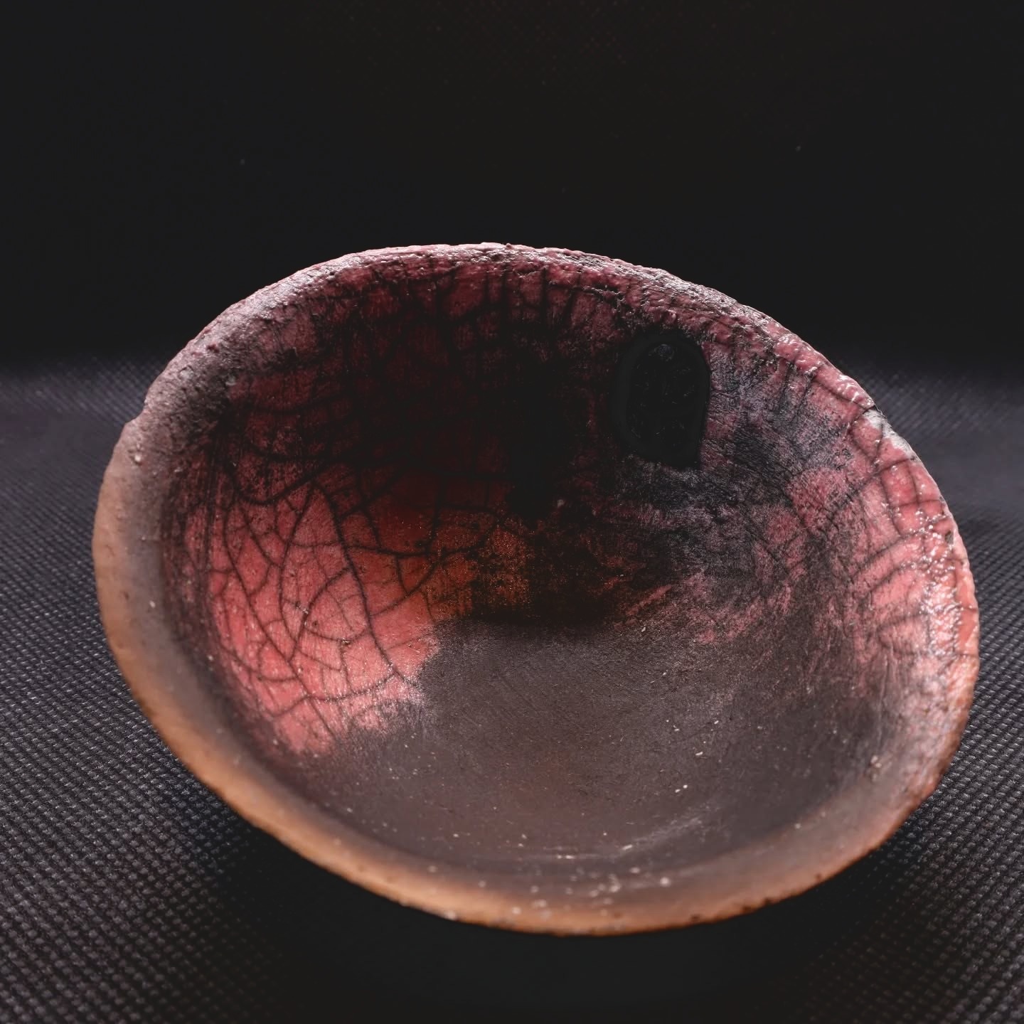 Finished red and copper raku bowl against a deep charcoal background