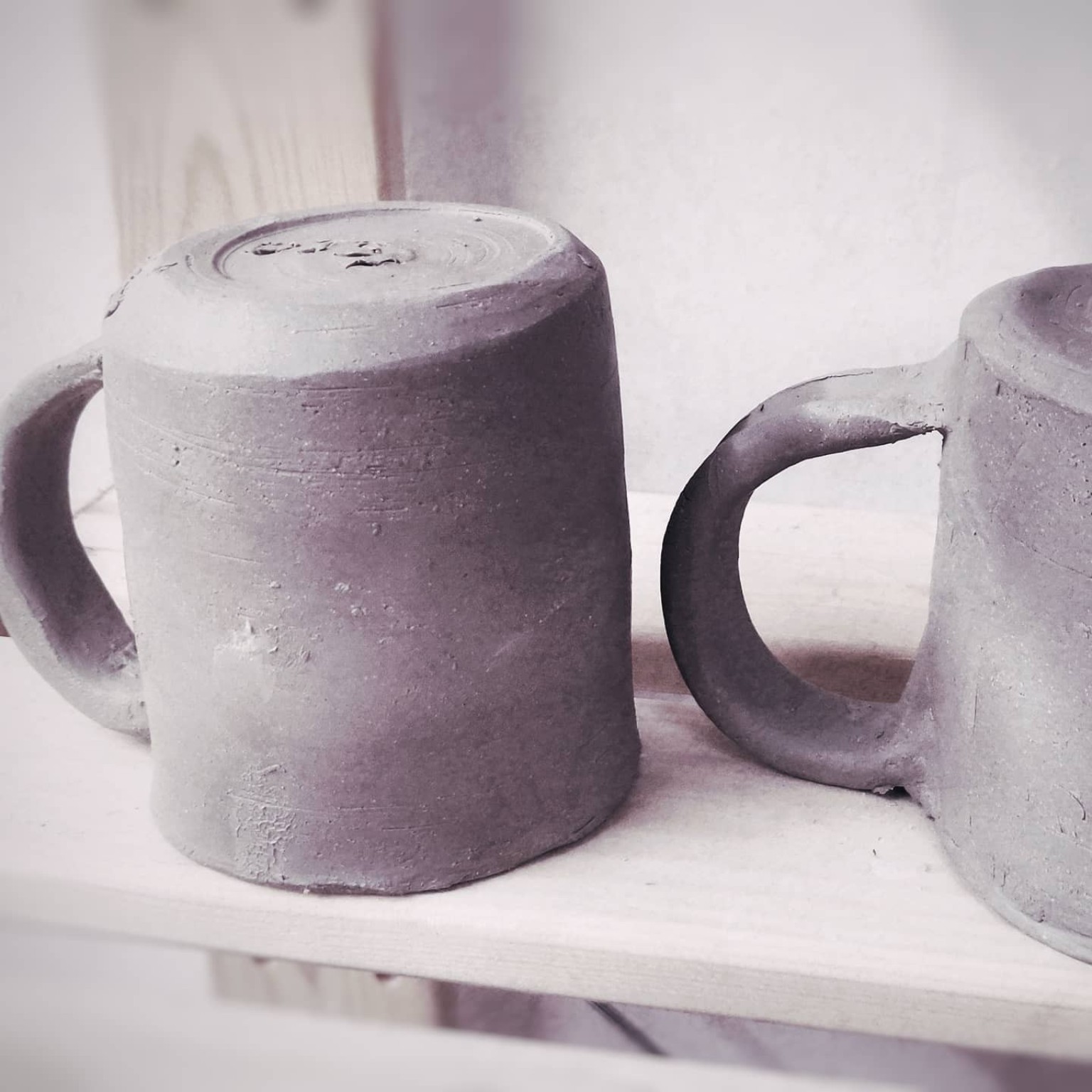 Two wheel-thrown mugs in progress before glazing and firing.