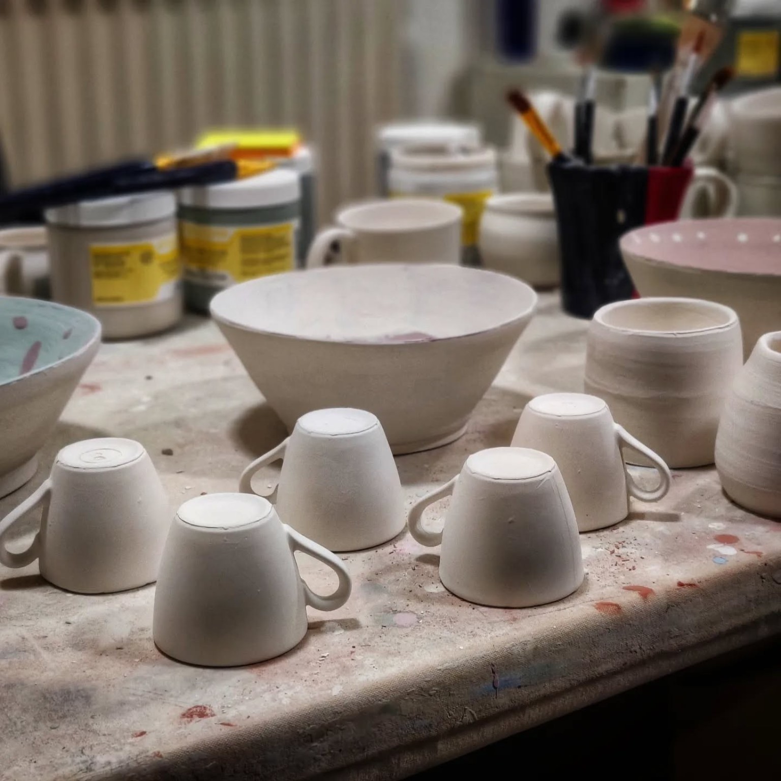Small batch of wheel-thrown studio mugs and bowls in progress on the workbench.