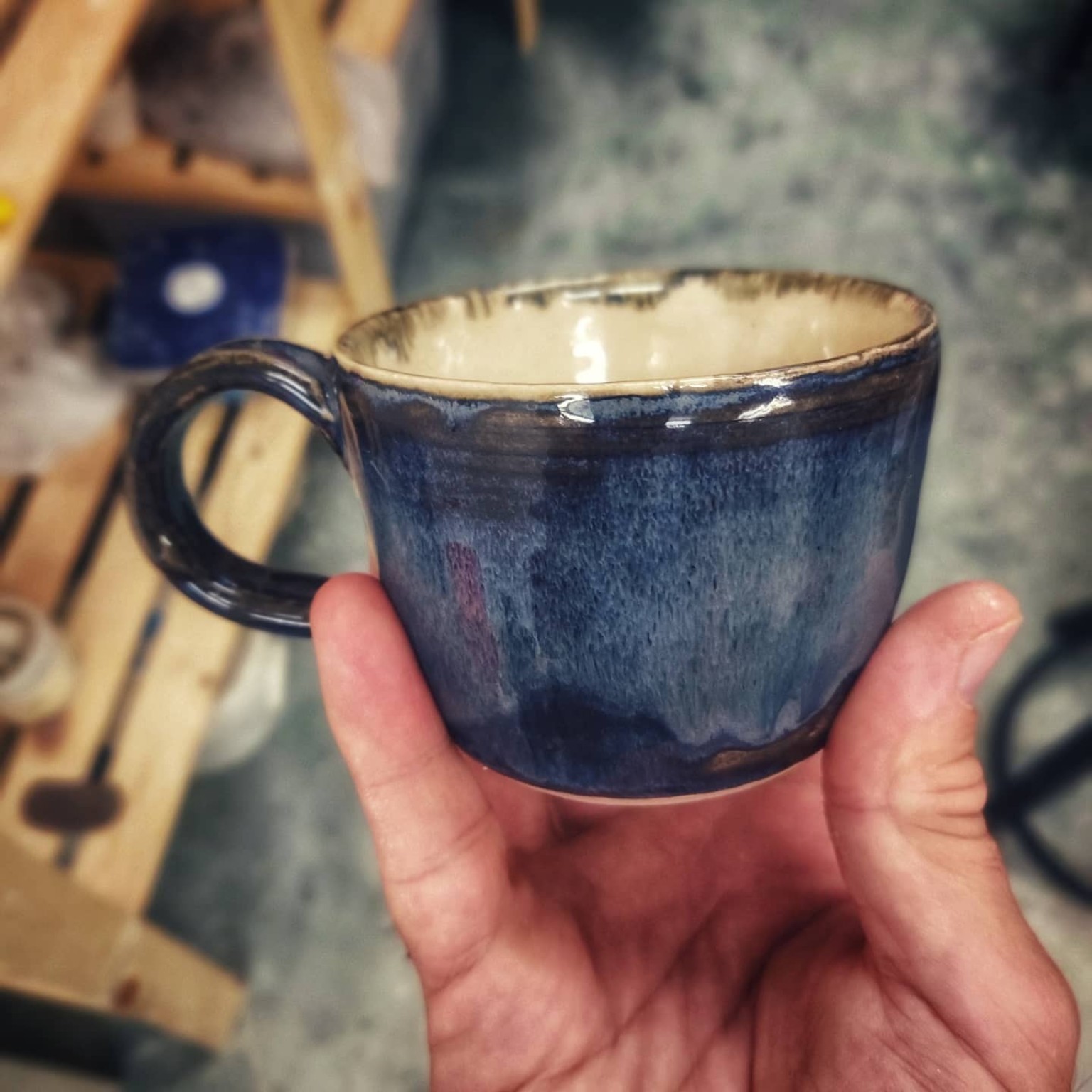 Blue glazed wheel-thrown studio espresso cup held in the hand.