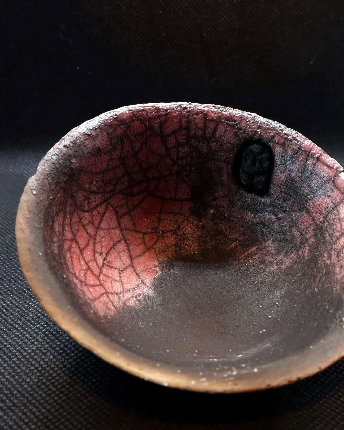 Low bowl viewed from above, with a pink-red crackle interior, darkened centre and small owl motif near the rim.
