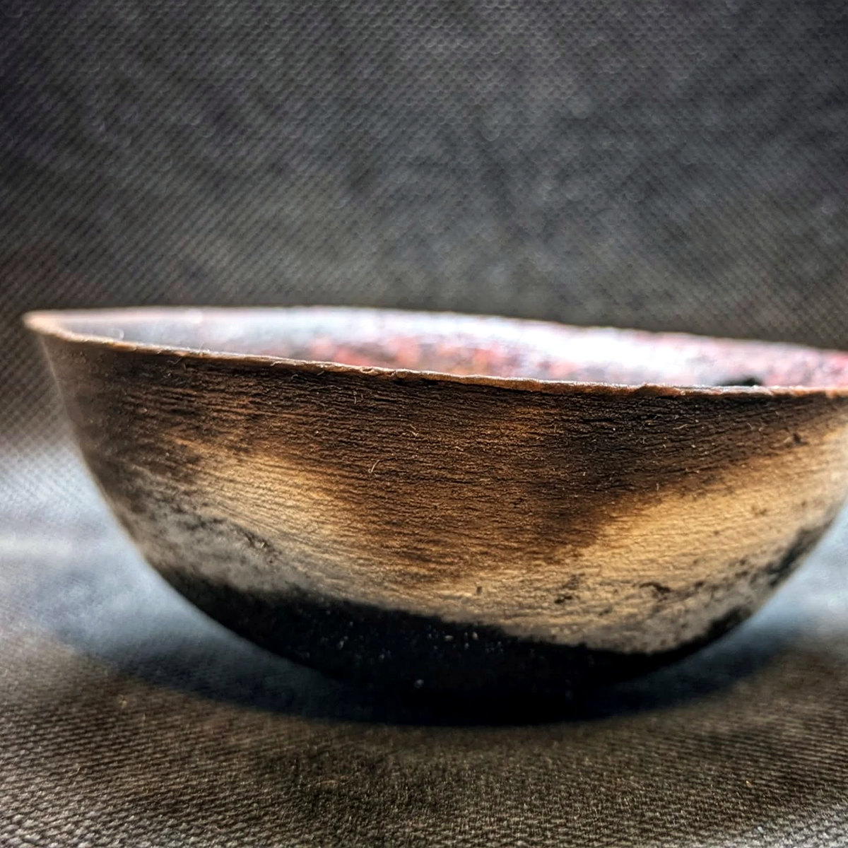 Side view of the same low bowl, showing its low profile and bronze-black exterior.