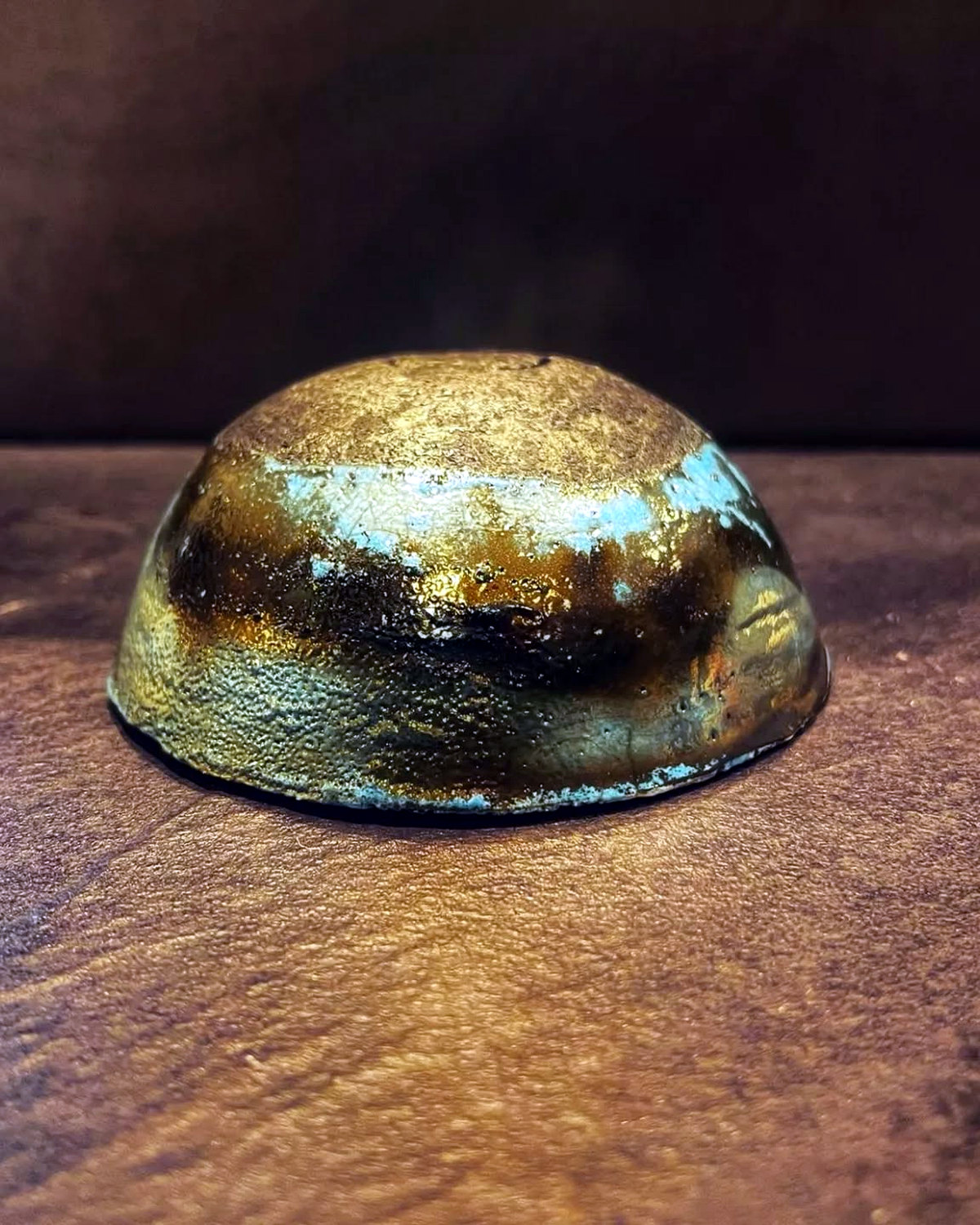Small raku jewellery bowl with a gold-bronze metallic surface, turquoise flashes and dark firing marks.