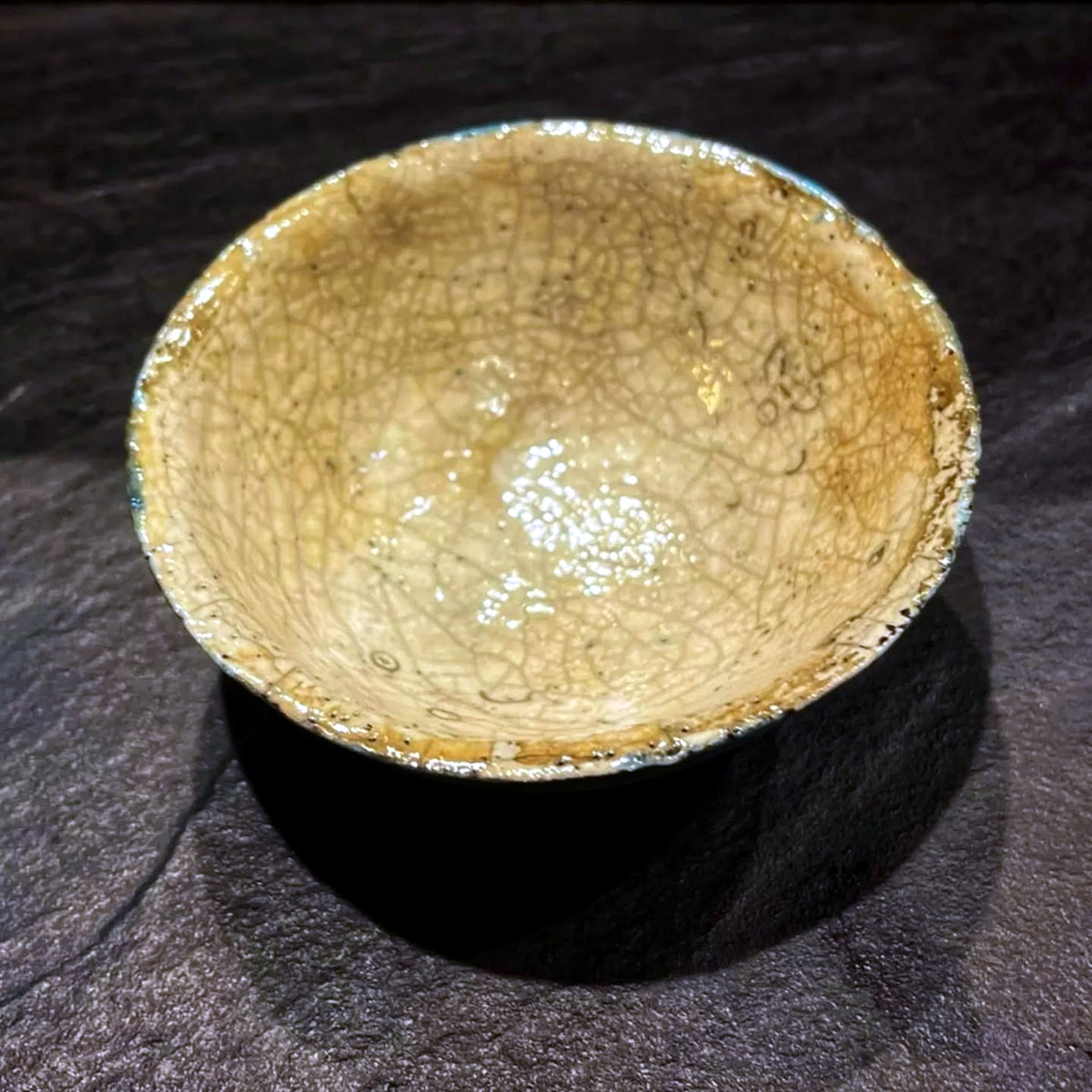 Interior view of the same jewellery bowl, showing a pale gold crackle surface and turquoise-blue edge along the irregular rim.