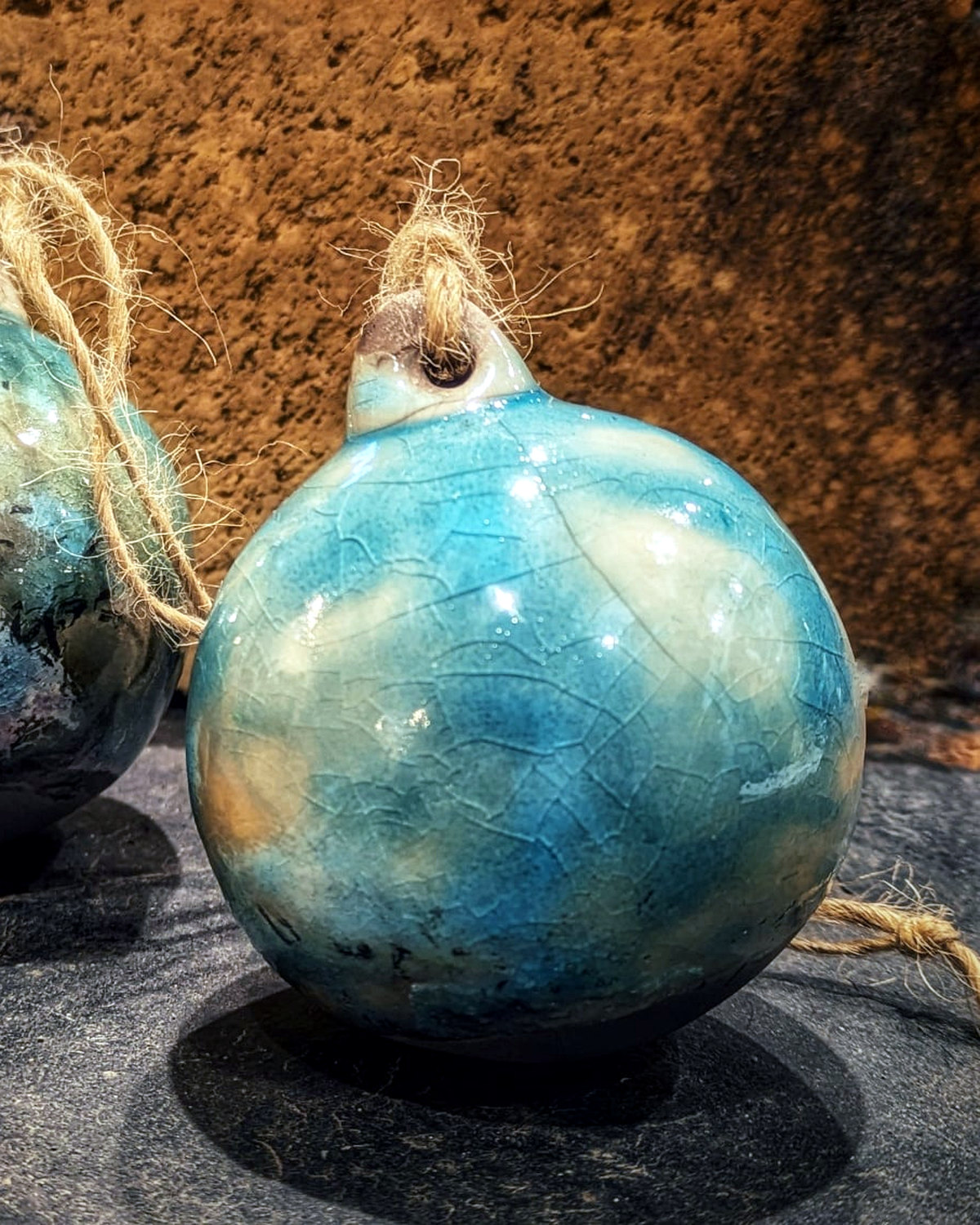 Detail of one blue-green raku Christmas tree bauble with a crackled surface and rustic twine loop.