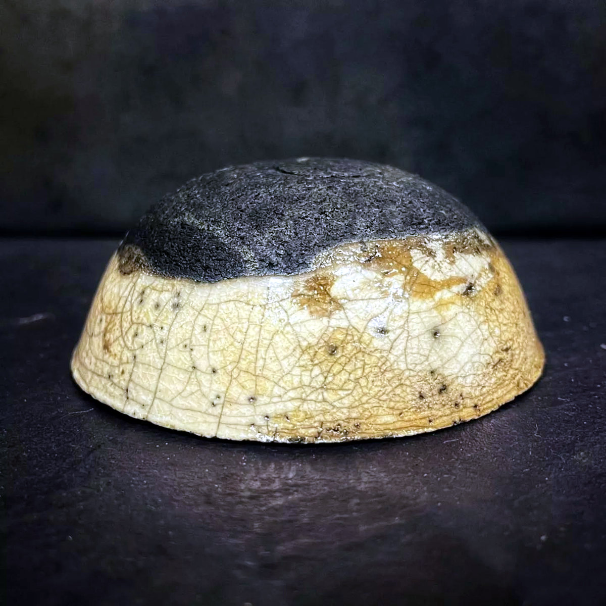 Full square view of the same decorative bowl, showing its pale crackle surface, dark upper area and fired marks.