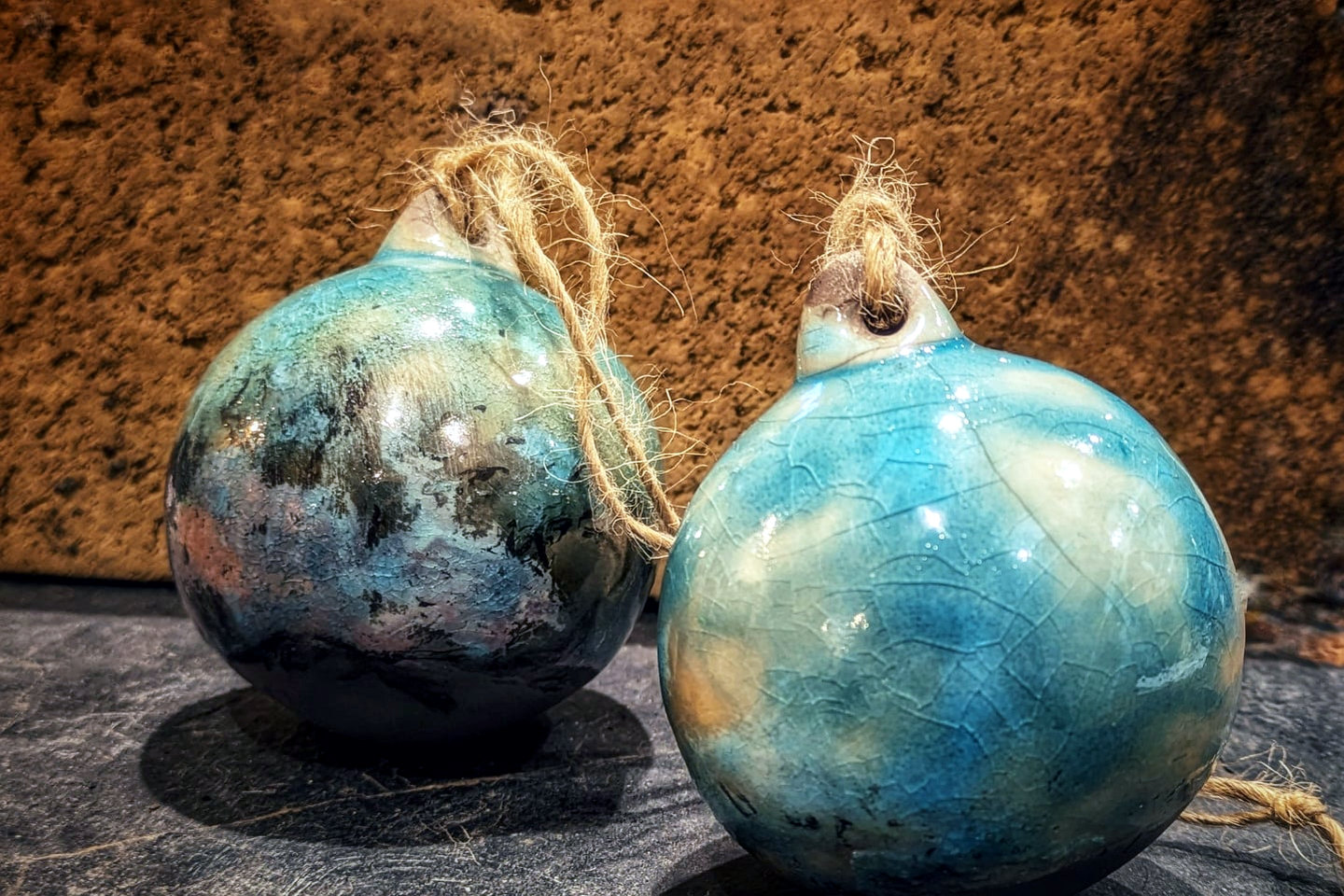 Pair of blue-green raku Christmas tree baubles with crackled surfaces and rustic twine loops.