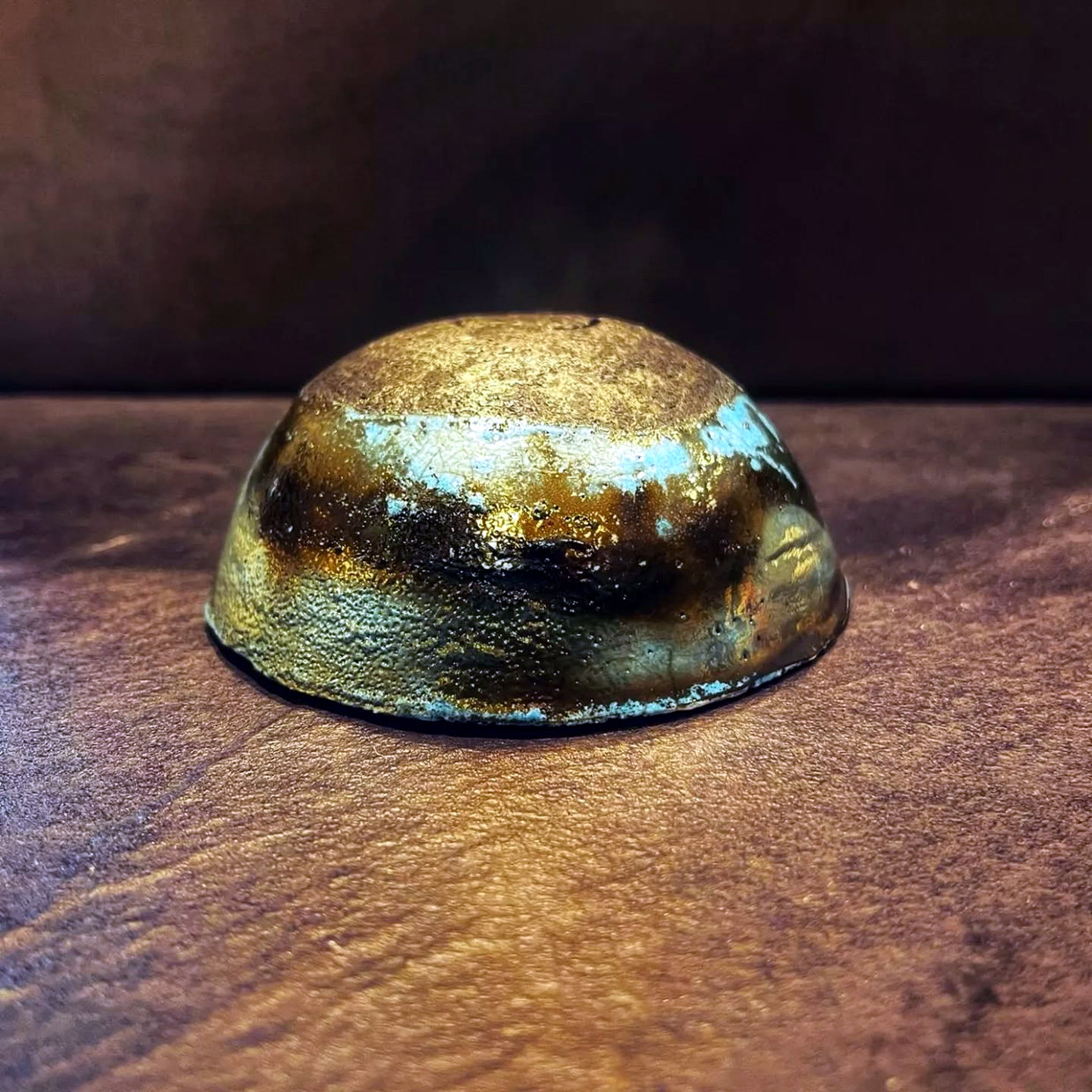 Small raku jewellery bowl with a gold-bronze metallic surface, turquoise flashes and dark firing marks.
