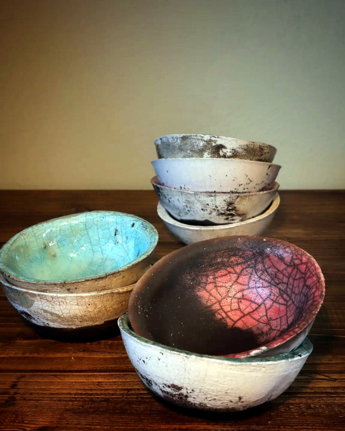 Grouped small ceramic bowls, including turquoise and pink crackle-glazed pieces with a stack of pale fired bowls behind.